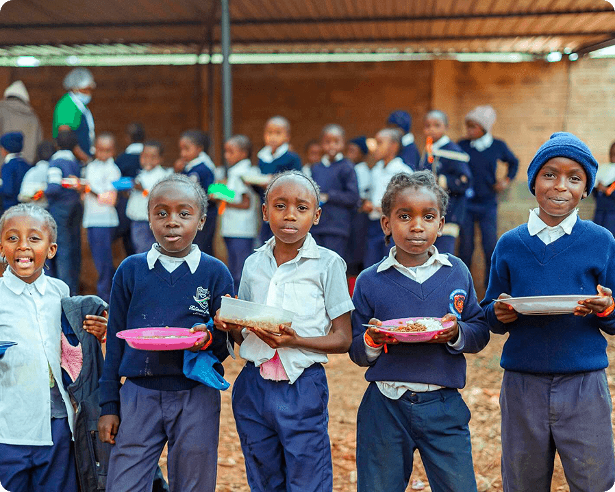 Five young boys standing in a line, holding their plates out in front of them