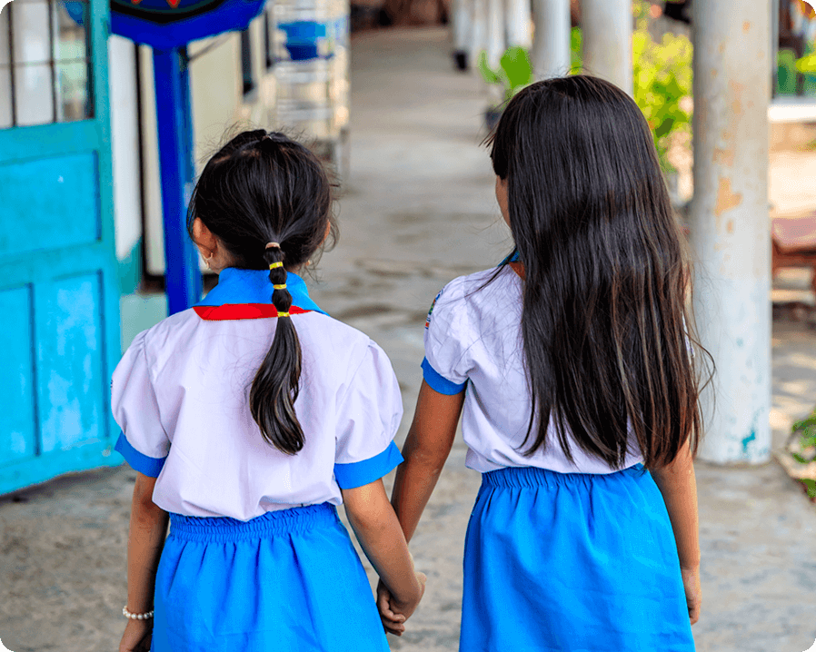 Two little girls in dresses, holding hands, walking to school