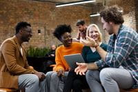 Group of smiling people in a room. One has a laptop on her lap.