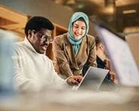 Two students collaborate on a laptop in a university learning space.