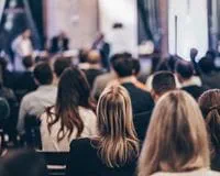 Attendees listen to a speaker at a professional event.